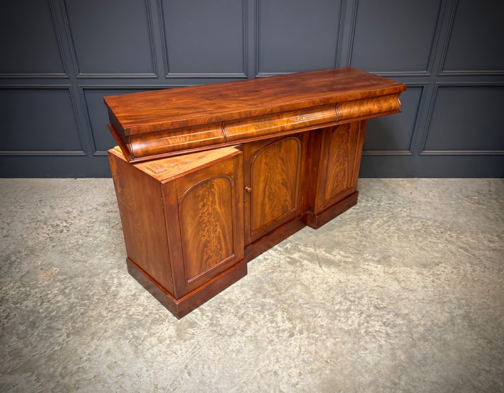 A Victorian mahogany sideboard featuring three flame mahogany veneer arched panel doors and concealed frieze drawers set on a plinth base. View III