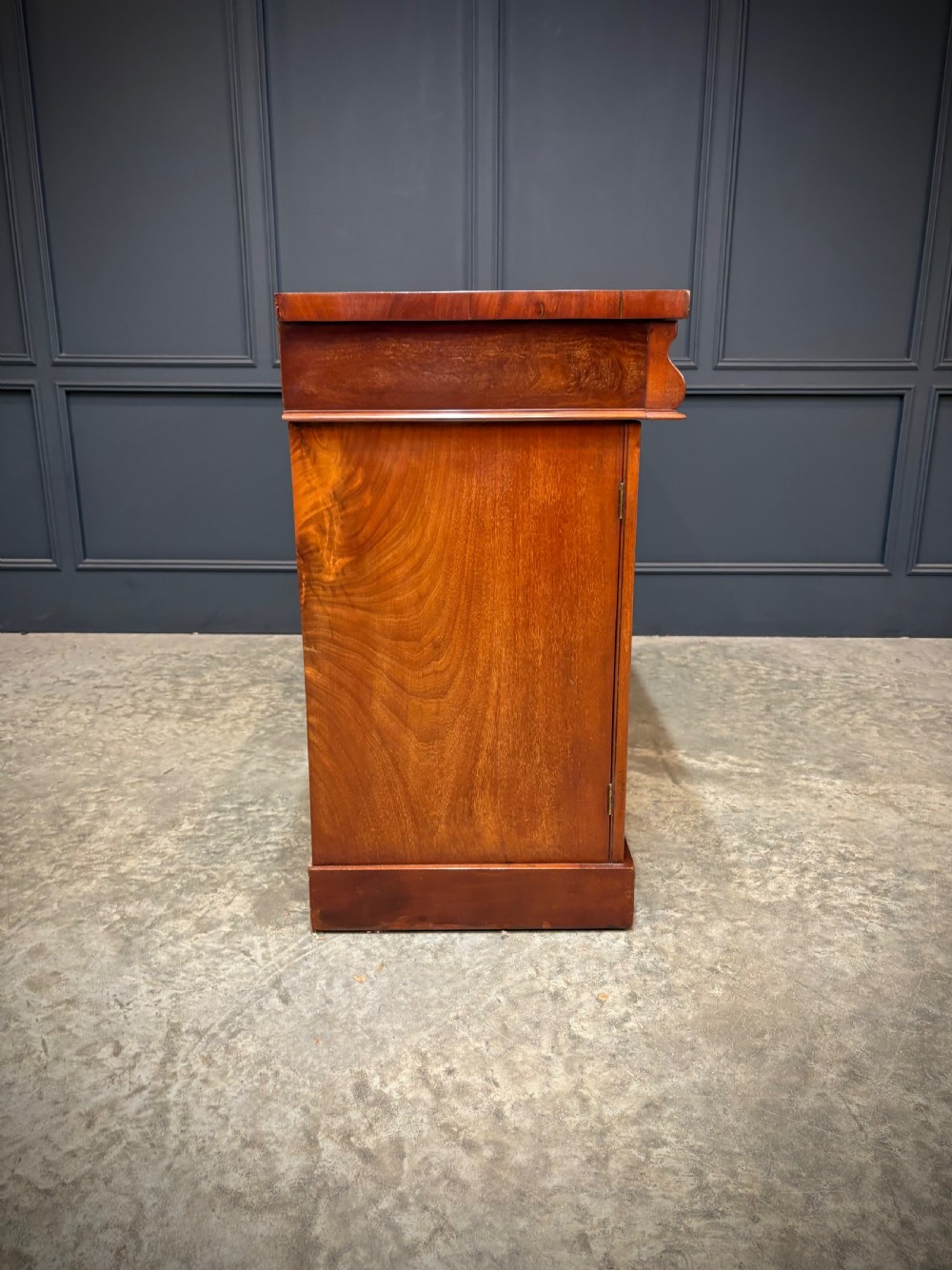 A Victorian mahogany sideboard featuring three flame mahogany veneer arched panel doors and concealed frieze drawers set on a plinth base. View XII