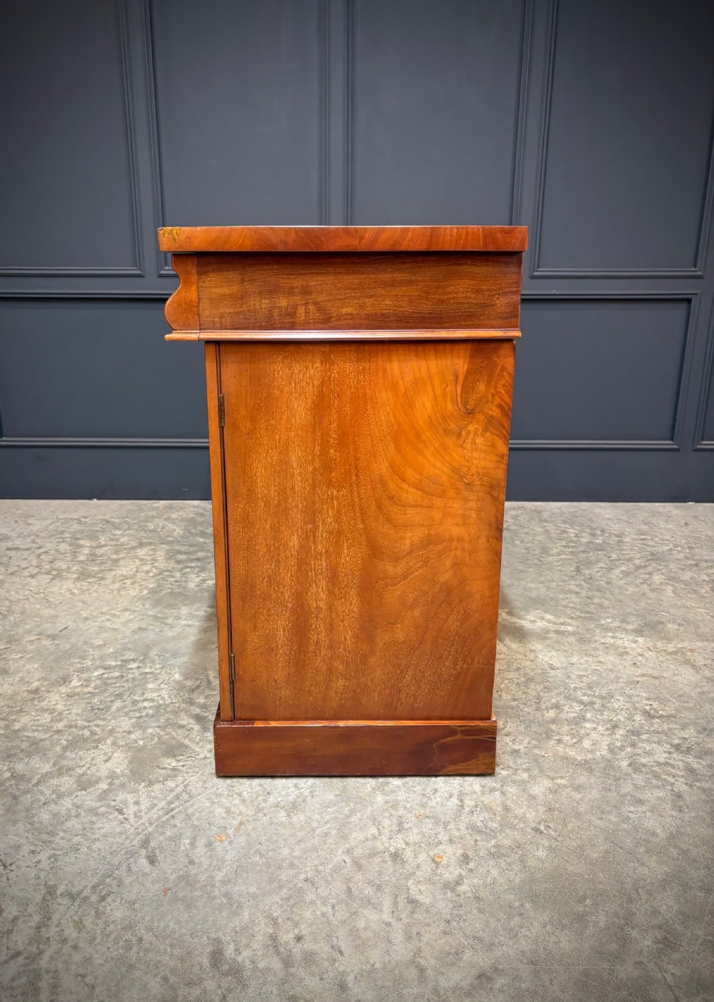 A Victorian mahogany sideboard featuring three flame mahogany veneer arched panel doors and concealed frieze drawers set on a plinth base. View XIII