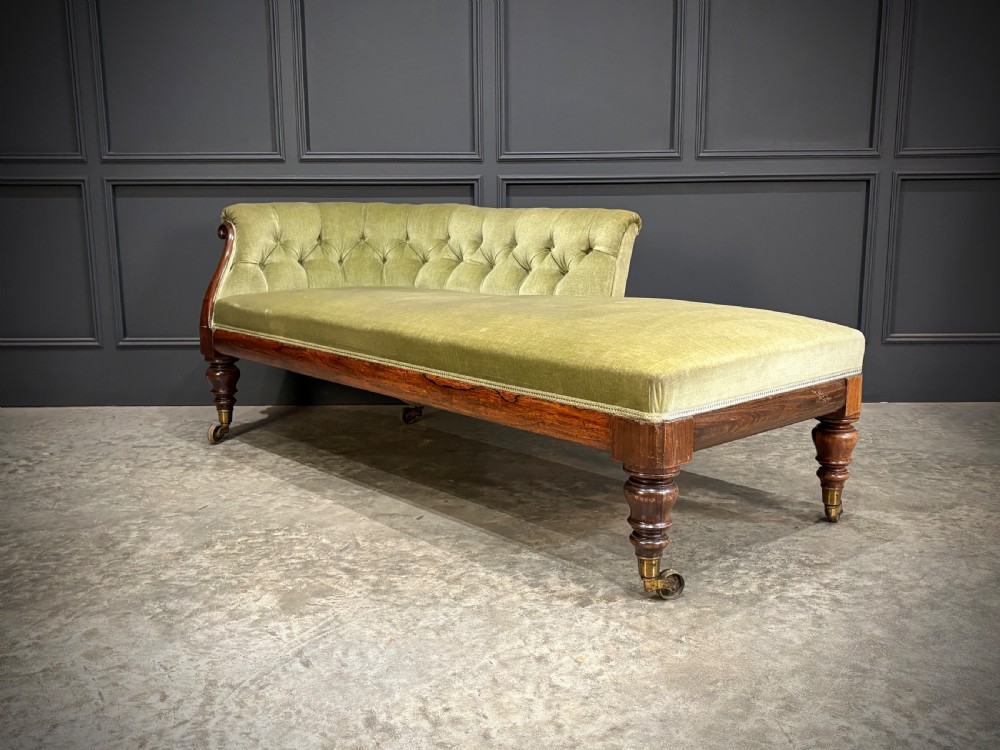 A Victorian rosewood chaise longue upholstered in olive green velvet with deep buttoning along the asymmetrical backrest, supported by turned legs on brass castors. View VI