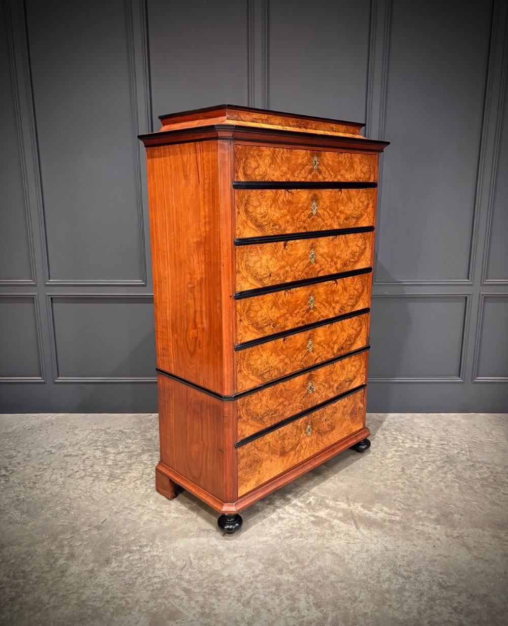 A tall 19th-century burr walnut chest of drawers featuring seven graduated drawers with brass escutcheons and ebonised mouldings set on turned front feet. View II