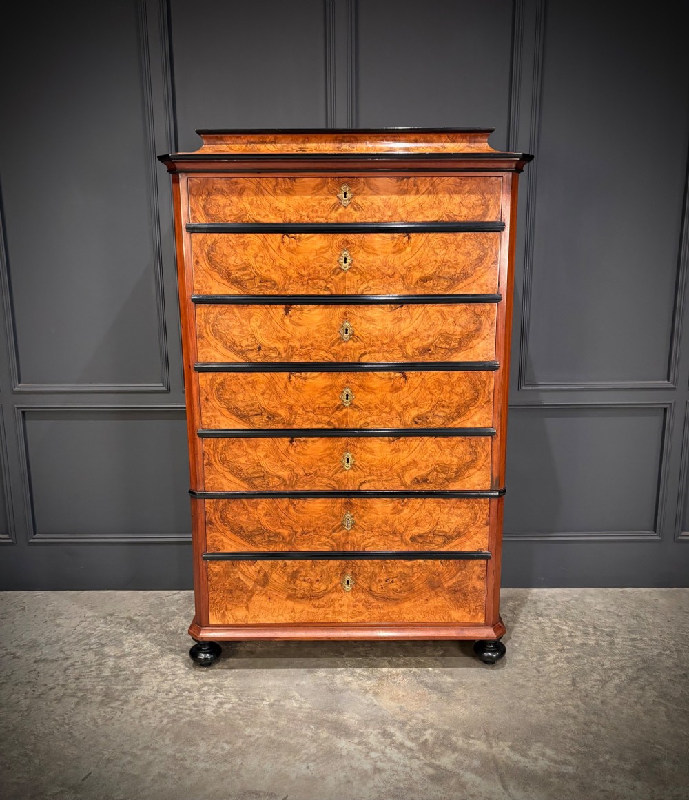 A tall 19th-century burr walnut chest of drawers featuring seven graduated drawers with brass escutcheons and ebonised mouldings set on turned front feet. View V