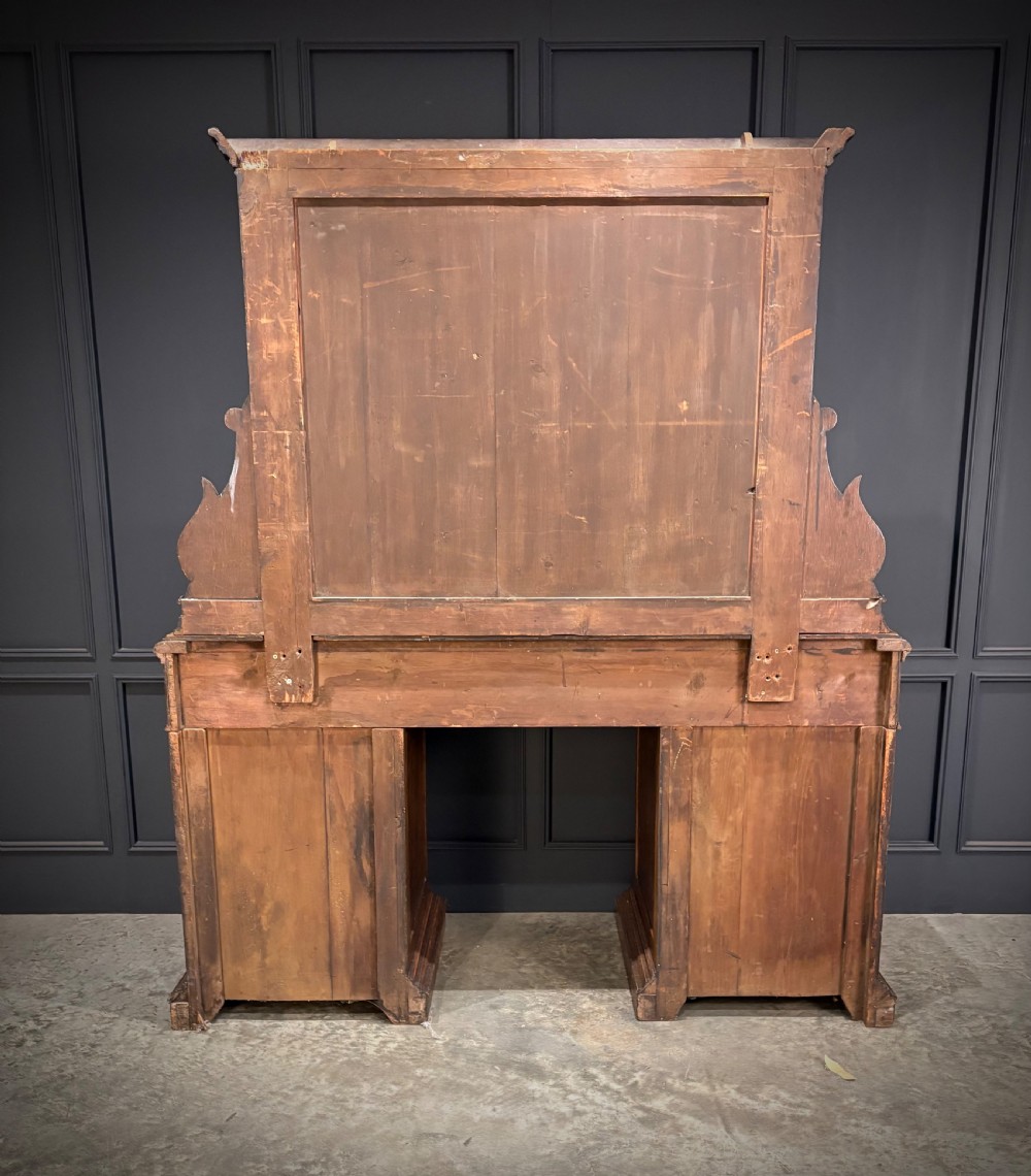 A dark carved oak sideboard featuring a upper mirror frame with floral carving above a pedestal base with relief carved cupboard doors. View III