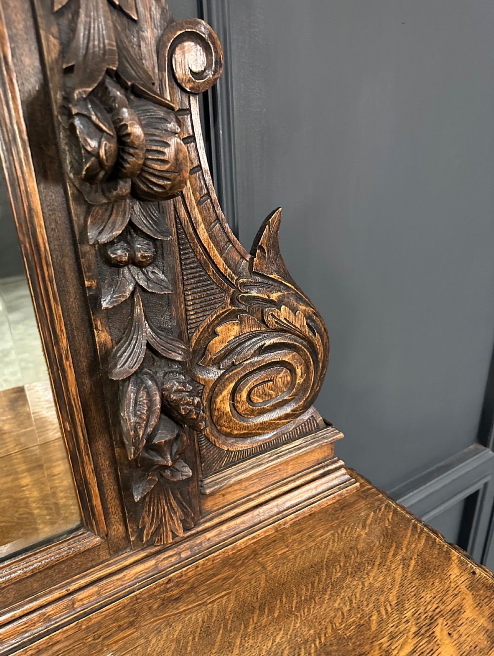 A dark carved oak sideboard featuring a upper mirror frame with floral carving above a pedestal base with relief carved cupboard doors. View IX