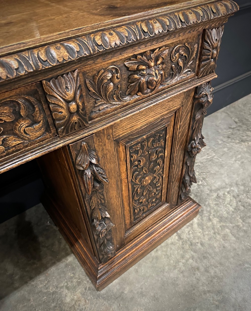 A dark carved oak sideboard featuring a upper mirror frame with floral carving above a pedestal base with relief carved cupboard doors. View X