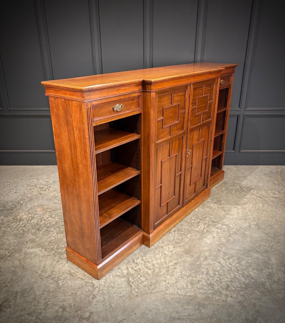 A low breakfront walnut bookcase featuring a central two-door cupboard flanked by open shelves and top drawers with brass handles. View III