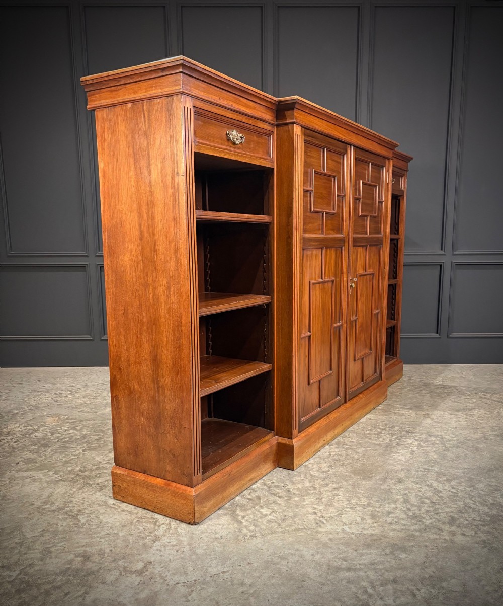 A low breakfront walnut bookcase featuring a central two-door cupboard flanked by open shelves and top drawers with brass handles. View II
