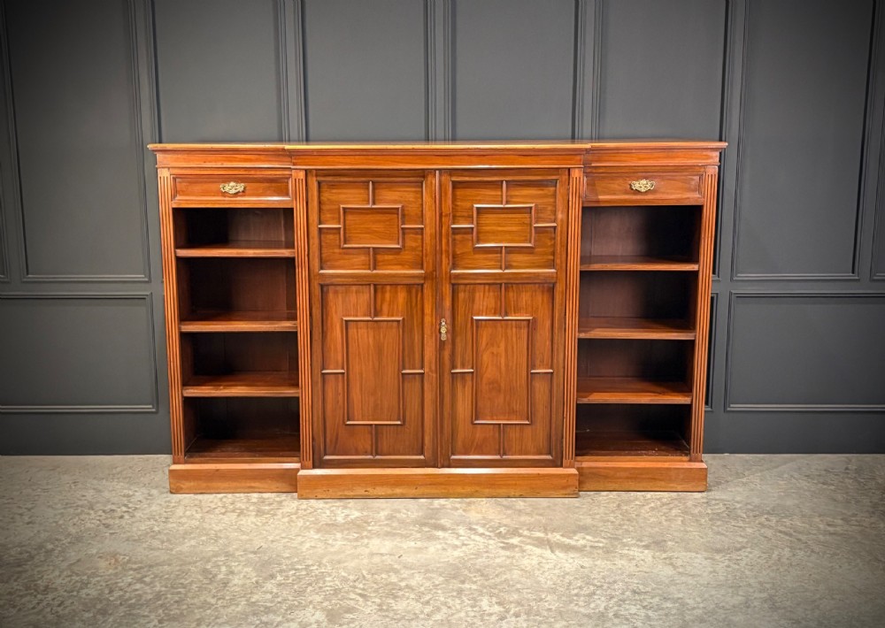 A low breakfront walnut bookcase featuring a central two-door cupboard flanked by open shelves and top drawers with brass handles.