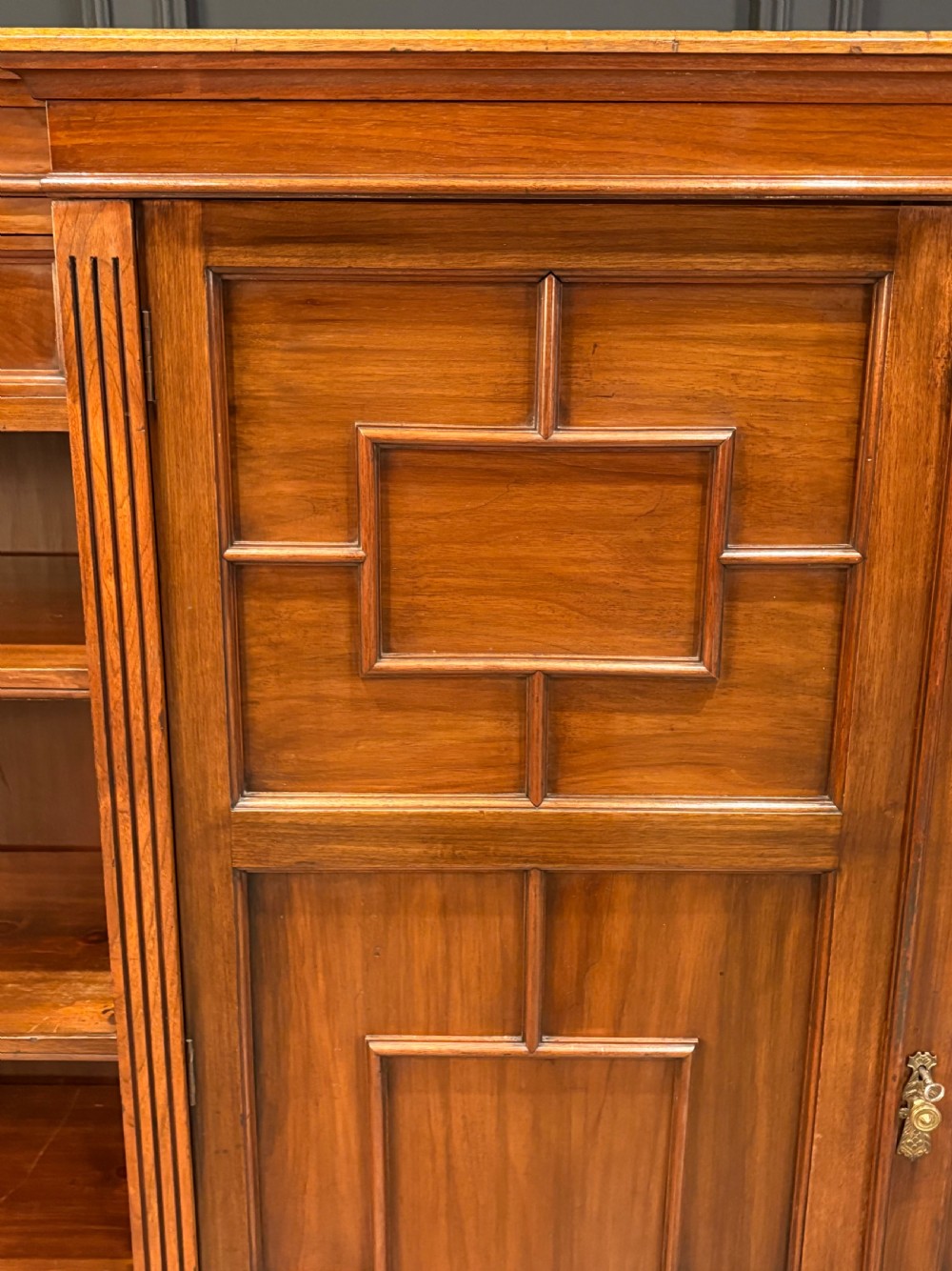 A low breakfront walnut bookcase featuring a central two-door cupboard flanked by open shelves and top drawers with brass handles. View VI