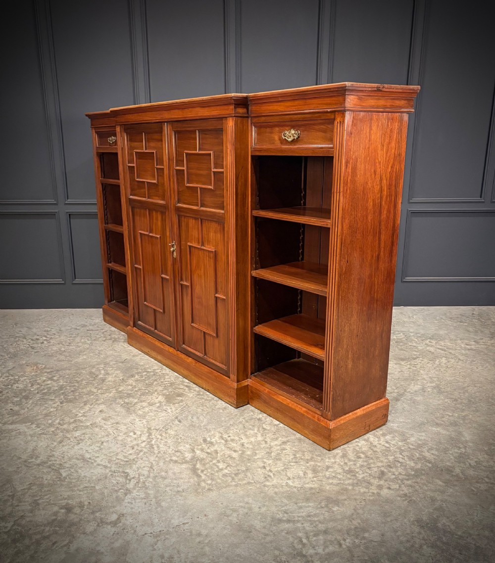 A low breakfront walnut bookcase featuring a central two-door cupboard flanked by open shelves and top drawers with brass handles. View IX