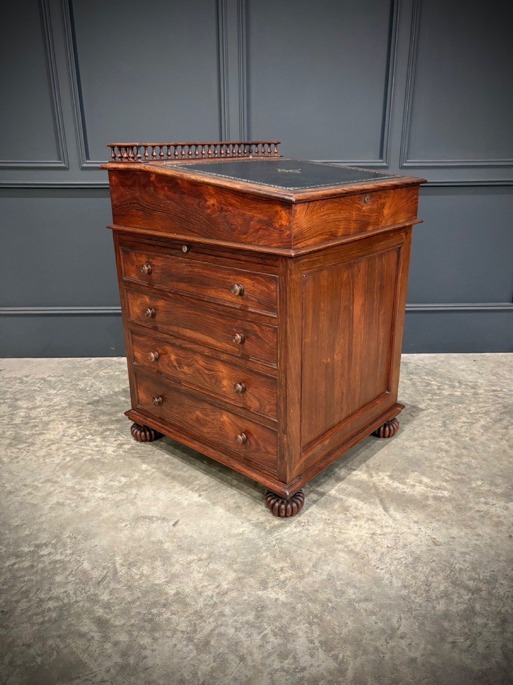 A 19th-century rosewood Davenport desk featuring a sloped writing top inset with dark green tooled leather, a spindled gallery rail, and stacked drawers. View II