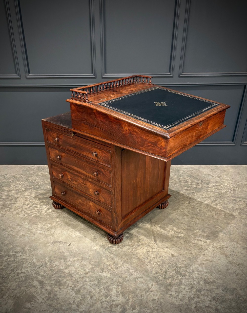 A 19th-century rosewood Davenport desk featuring a sloped writing top inset with dark green tooled leather, a spindled gallery rail, and stacked drawers. View III