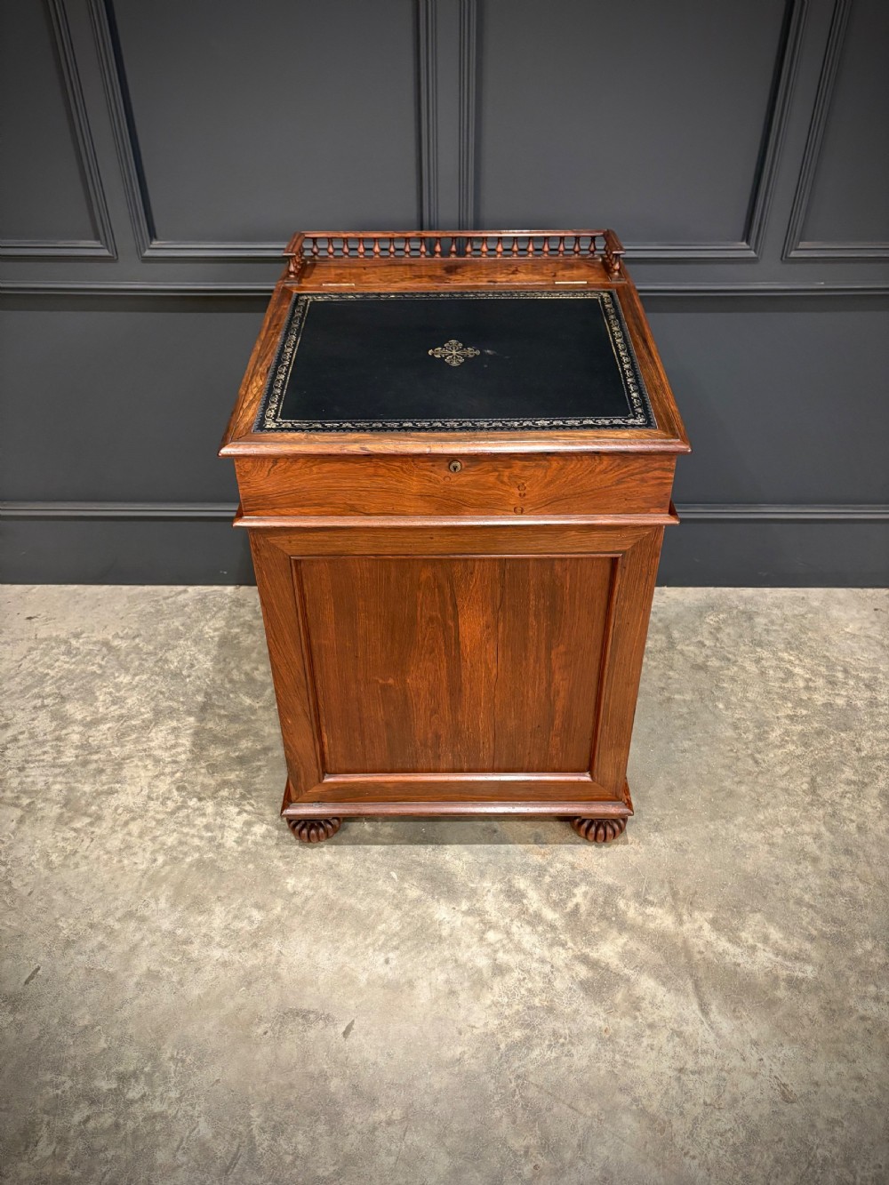 A 19th-century rosewood Davenport desk featuring a sloped writing top inset with dark green tooled leather, a spindled gallery rail, and stacked drawers. View IV