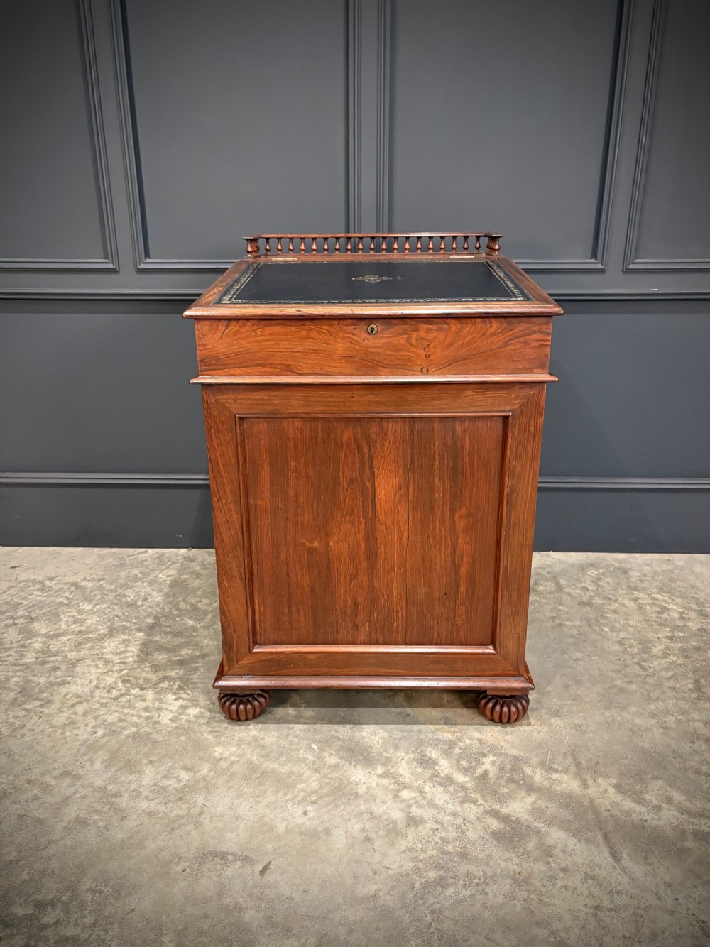 A 19th-century rosewood Davenport desk featuring a sloped writing top inset with dark green tooled leather, a spindled gallery rail, and stacked drawers. View V