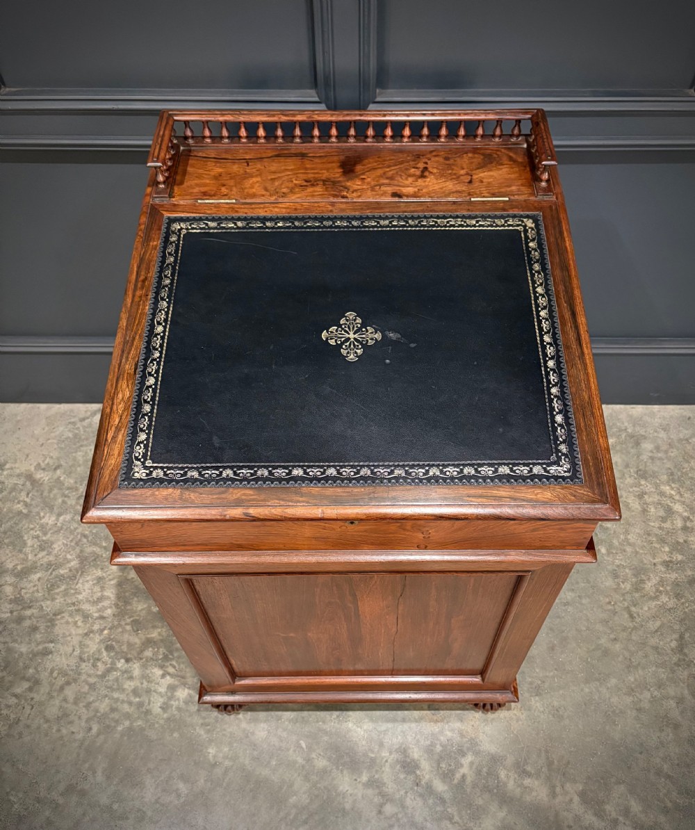 A 19th-century rosewood Davenport desk featuring a sloped writing top inset with dark green tooled leather, a spindled gallery rail, and stacked drawers. View VI