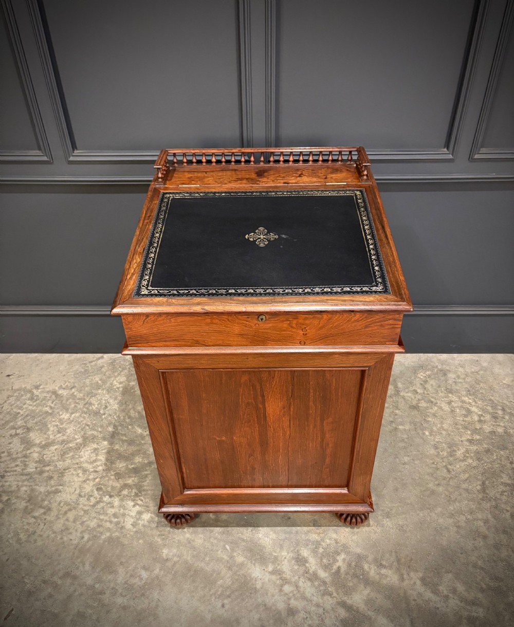 A 19th-century rosewood Davenport desk featuring a sloped writing top inset with dark green tooled leather, a spindled gallery rail, and stacked drawers. View IX