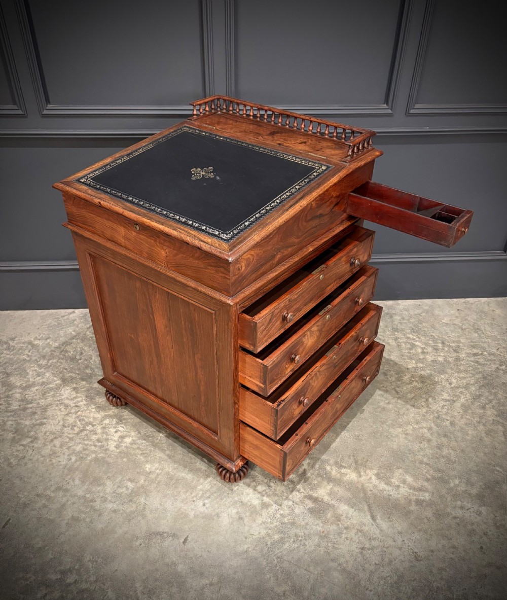 A 19th-century rosewood Davenport desk featuring a sloped writing top inset with dark green tooled leather, a spindled gallery rail, and stacked drawers. View XI