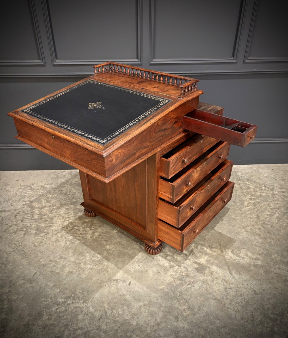 A 19th-century rosewood Davenport desk featuring a sloped writing top inset with dark green tooled leather, a spindled gallery rail, and stacked drawers. View XII