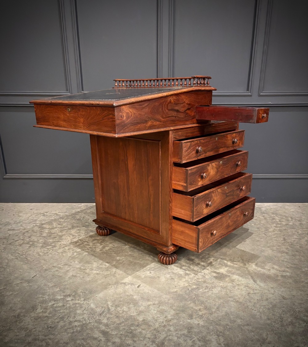 A 19th-century rosewood Davenport desk featuring a sloped writing top inset with dark green tooled leather, a spindled gallery rail, and stacked drawers. View XIII