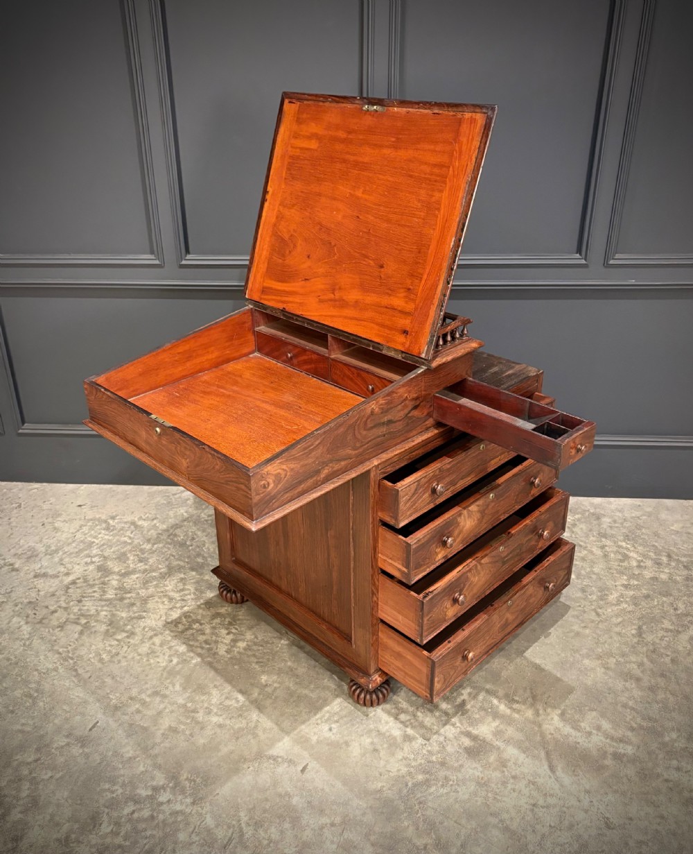 A 19th-century rosewood Davenport desk featuring a sloped writing top inset with dark green tooled leather, a spindled gallery rail, and stacked drawers. View XIV