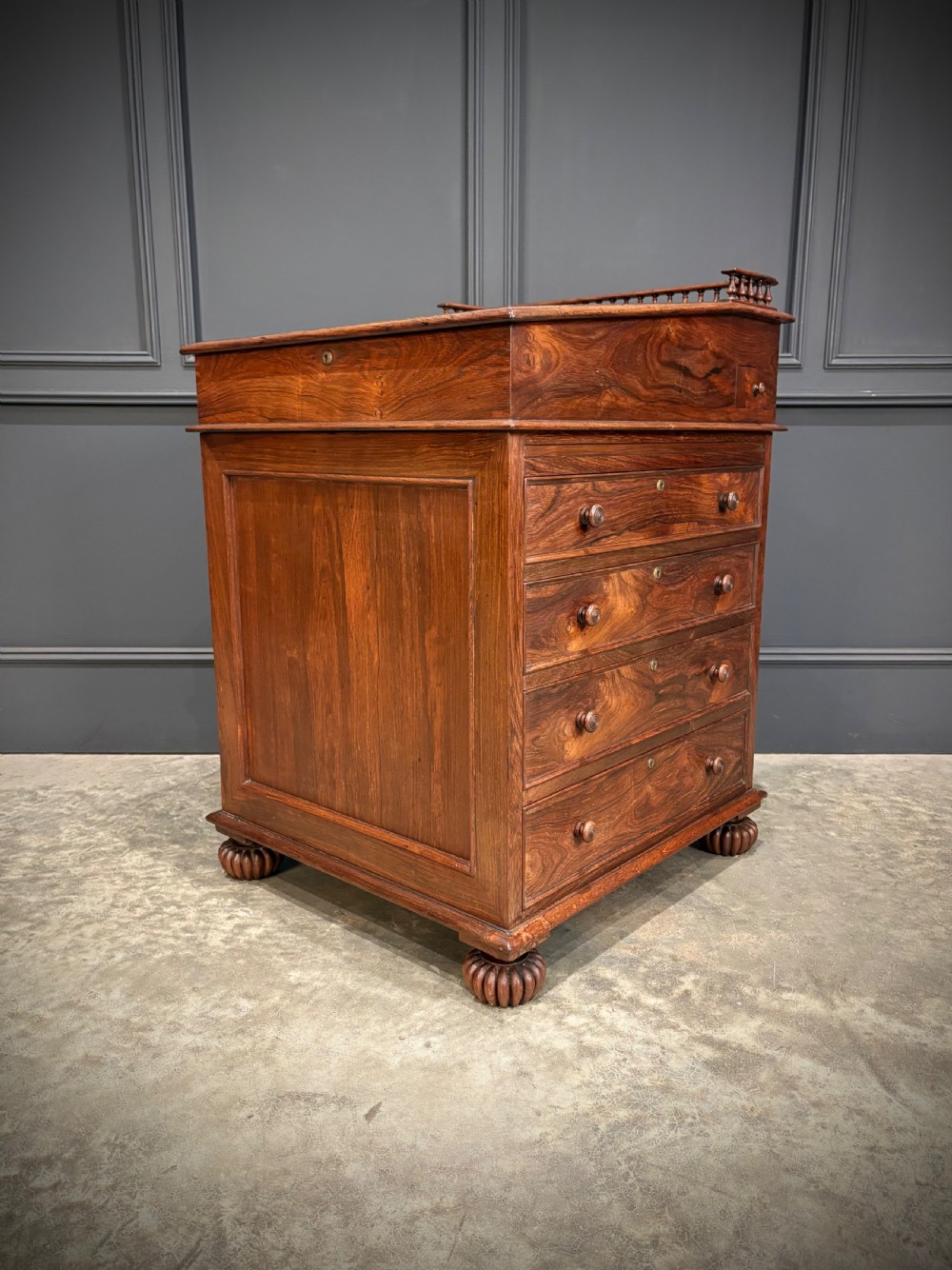 A 19th-century rosewood Davenport desk featuring a sloped writing top inset with dark green tooled leather, a spindled gallery rail, and stacked drawers. View XV