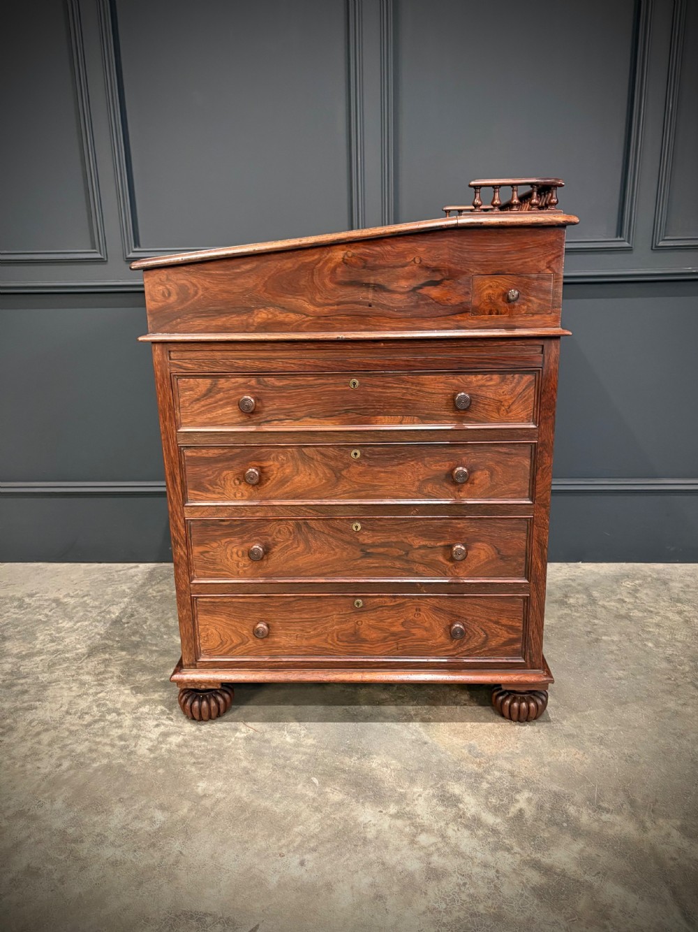 A 19th-century rosewood Davenport desk featuring a sloped writing top inset with dark green tooled leather, a spindled gallery rail, and stacked drawers. View XVI