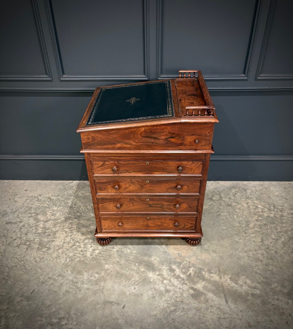 A 19th-century rosewood Davenport desk featuring a sloped writing top inset with dark green tooled leather, a spindled gallery rail, and stacked drawers. View XVII