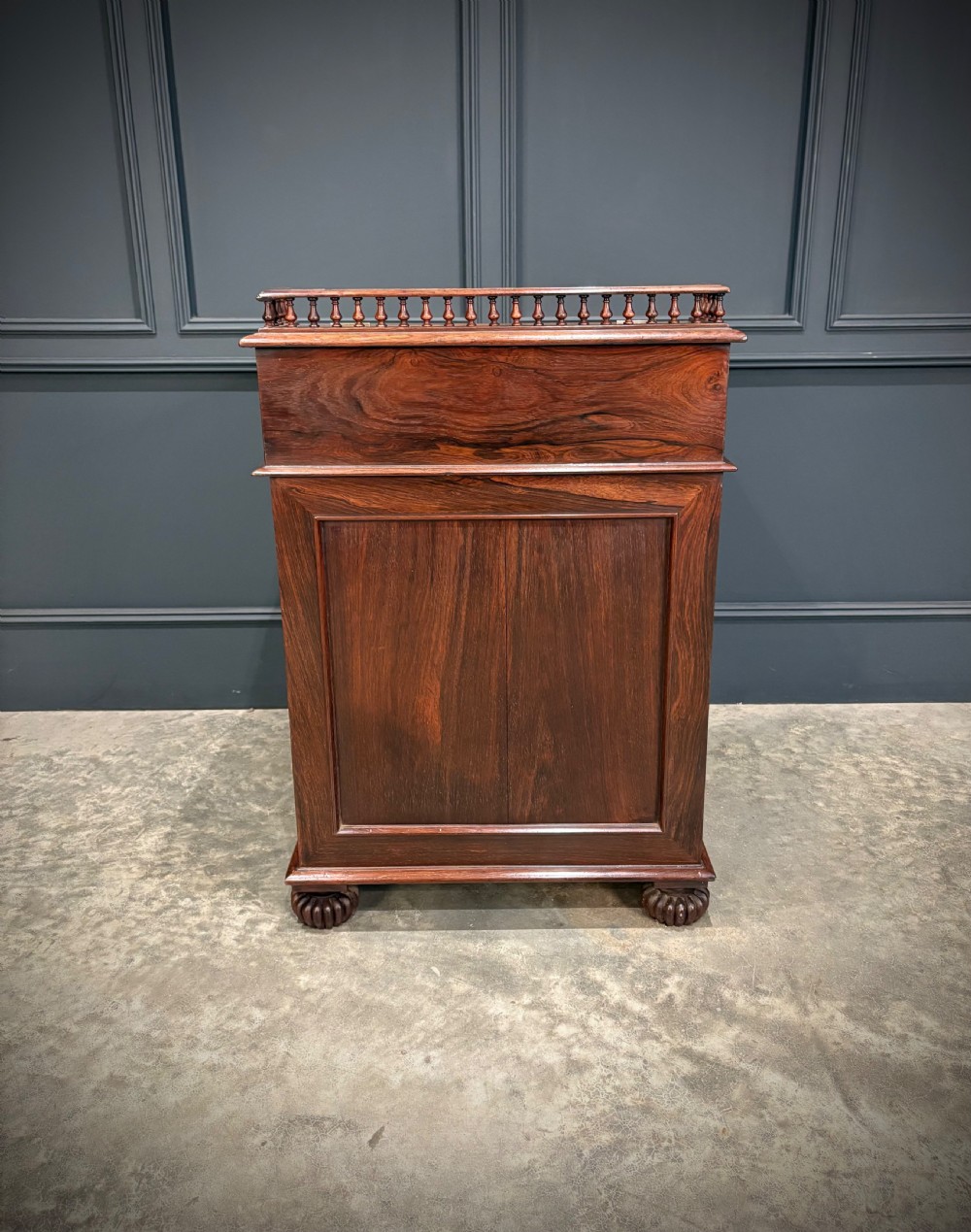 A 19th-century rosewood Davenport desk featuring a sloped writing top inset with dark green tooled leather, a spindled gallery rail, and stacked drawers. View XVIII