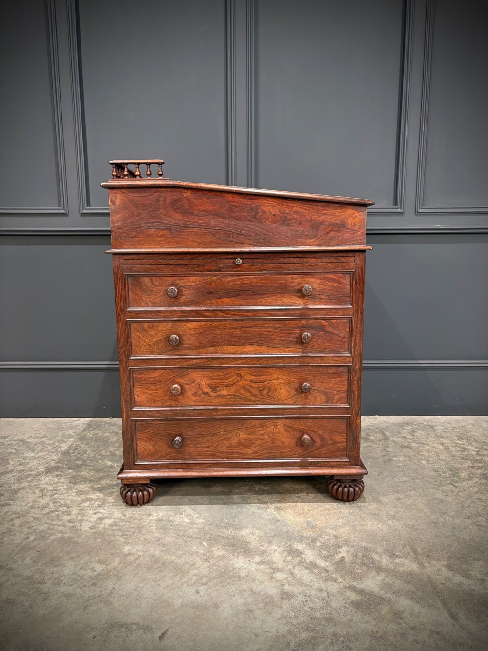 A 19th-century rosewood Davenport desk featuring a sloped writing top inset with dark green tooled leather, a spindled gallery rail, and stacked drawers. View XIX