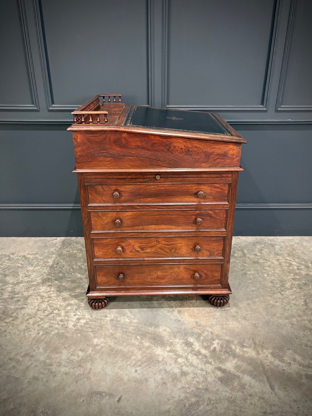 A 19th-century rosewood Davenport desk featuring a sloped writing top inset with dark green tooled leather, a spindled gallery rail, and stacked drawers. View XX