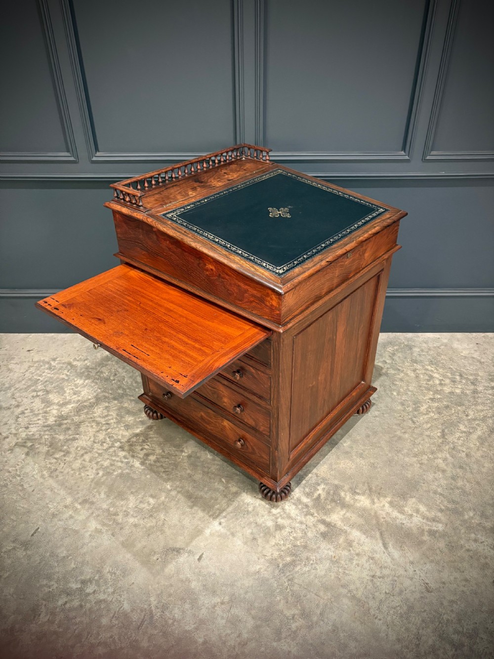 A 19th-century rosewood Davenport desk featuring a sloped writing top inset with dark green tooled leather, a spindled gallery rail, and stacked drawers. View XXI