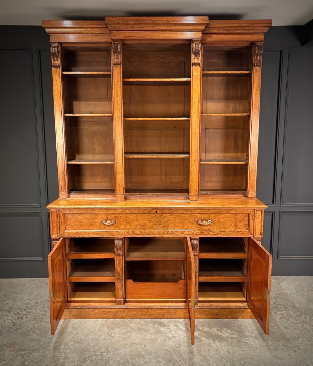 An early Victorian warm brown oak breakfront bookcase featuring glazed upper doors with arched tops, carved corbel accents, and a lower cabinet base. View II