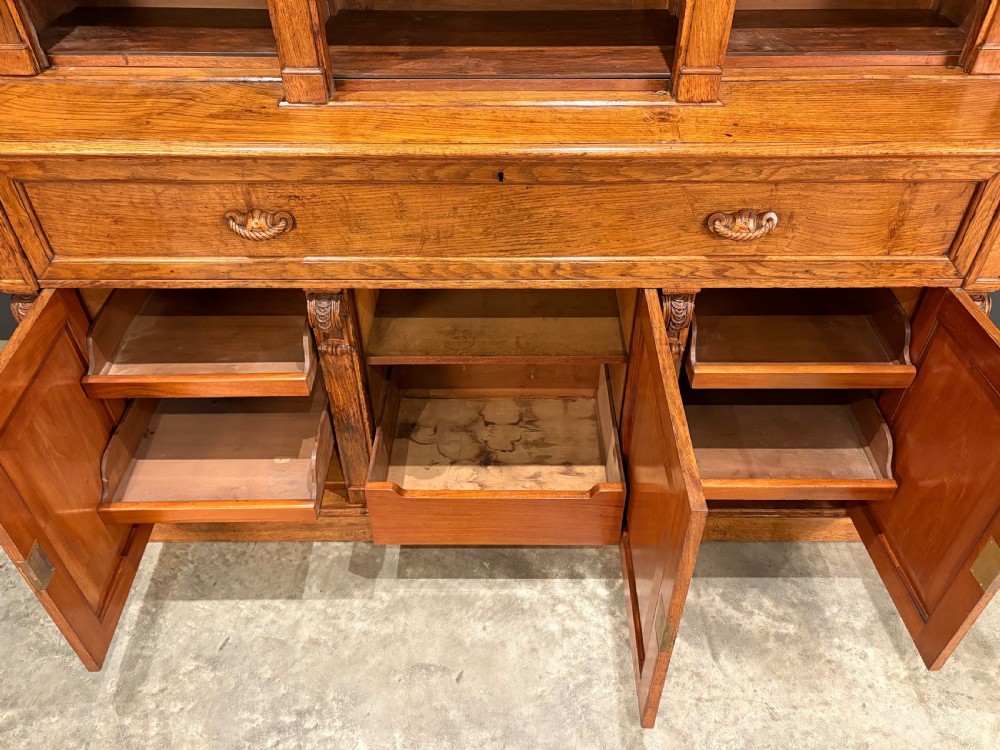 An early Victorian warm brown oak breakfront bookcase featuring glazed upper doors with arched tops, carved corbel accents, and a lower cabinet base. View III