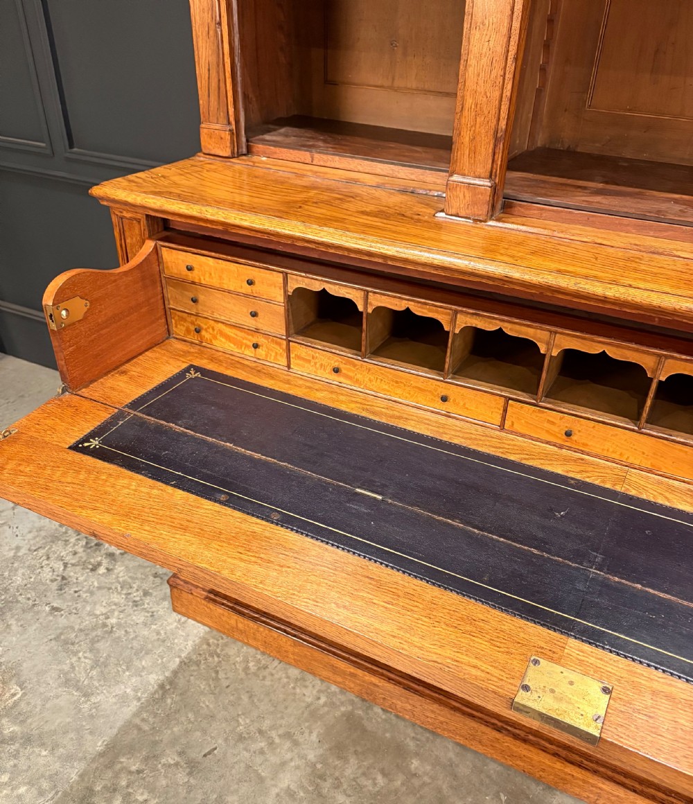 An early Victorian warm brown oak breakfront bookcase featuring glazed upper doors with arched tops, carved corbel accents, and a lower cabinet base. View VI