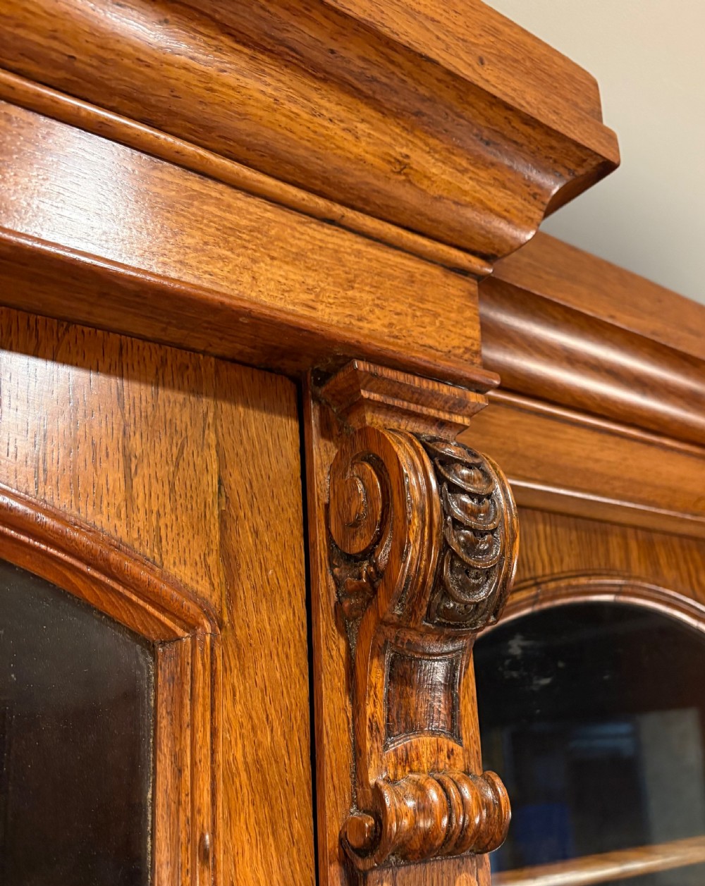 An early Victorian warm brown oak breakfront bookcase featuring glazed upper doors with arched tops, carved corbel accents, and a lower cabinet base. View IX