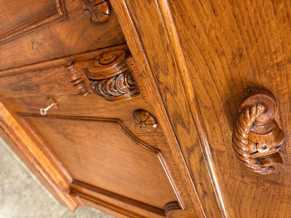 An early Victorian warm brown oak breakfront bookcase featuring glazed upper doors with arched tops, carved corbel accents, and a lower cabinet base. View X