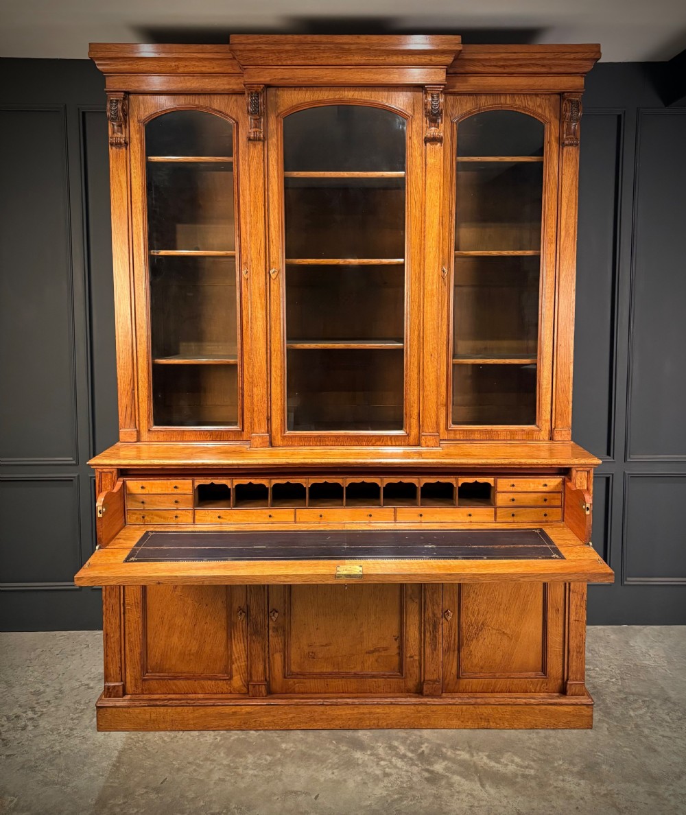 An early Victorian warm brown oak breakfront bookcase featuring glazed upper doors with arched tops, carved corbel accents, and a lower cabinet base. View XI
