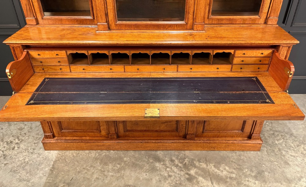 An early Victorian warm brown oak breakfront bookcase featuring glazed upper doors with arched tops, carved corbel accents, and a lower cabinet base. View XII