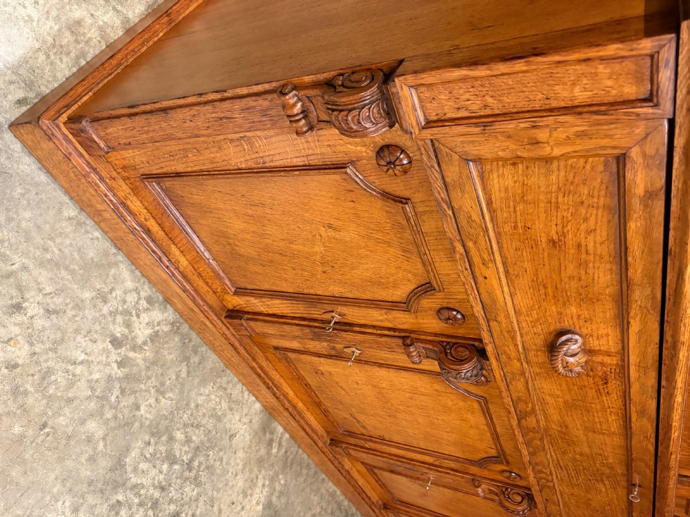An early Victorian warm brown oak breakfront bookcase featuring glazed upper doors with arched tops, carved corbel accents, and a lower cabinet base. View XIV