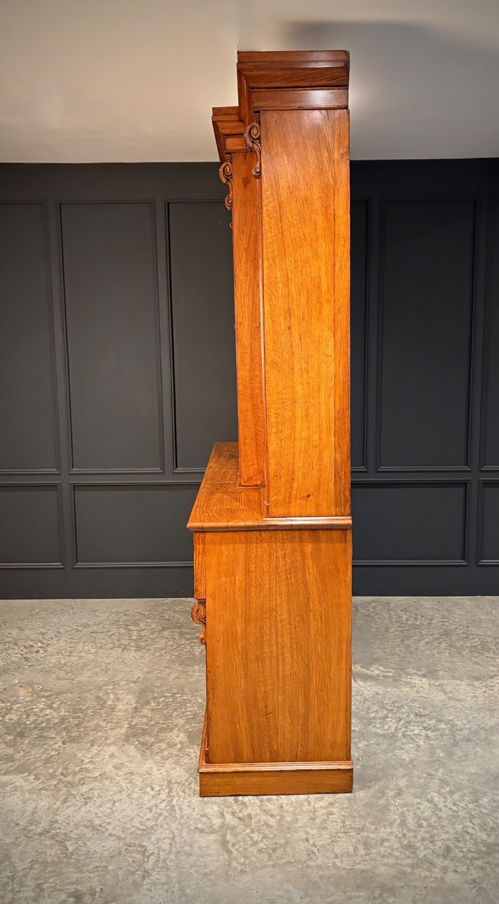 An early Victorian warm brown oak breakfront bookcase featuring glazed upper doors with arched tops, carved corbel accents, and a lower cabinet base. View XVII