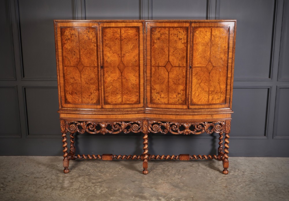 A double bow-front burr walnut cocktail cabinet featuring carved scrollwork on the lower apron, supported by six barley twist legs joined by stretchers.