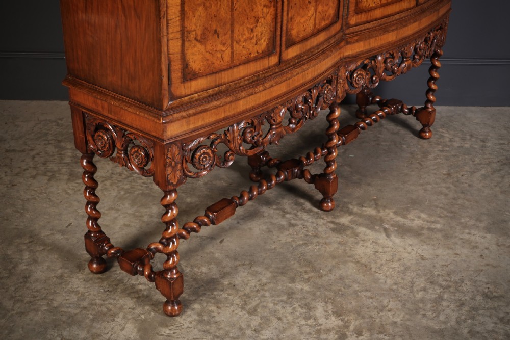 A double bow-front burr walnut cocktail cabinet featuring carved scrollwork on the lower apron, supported by six barley twist legs joined by stretchers. View II