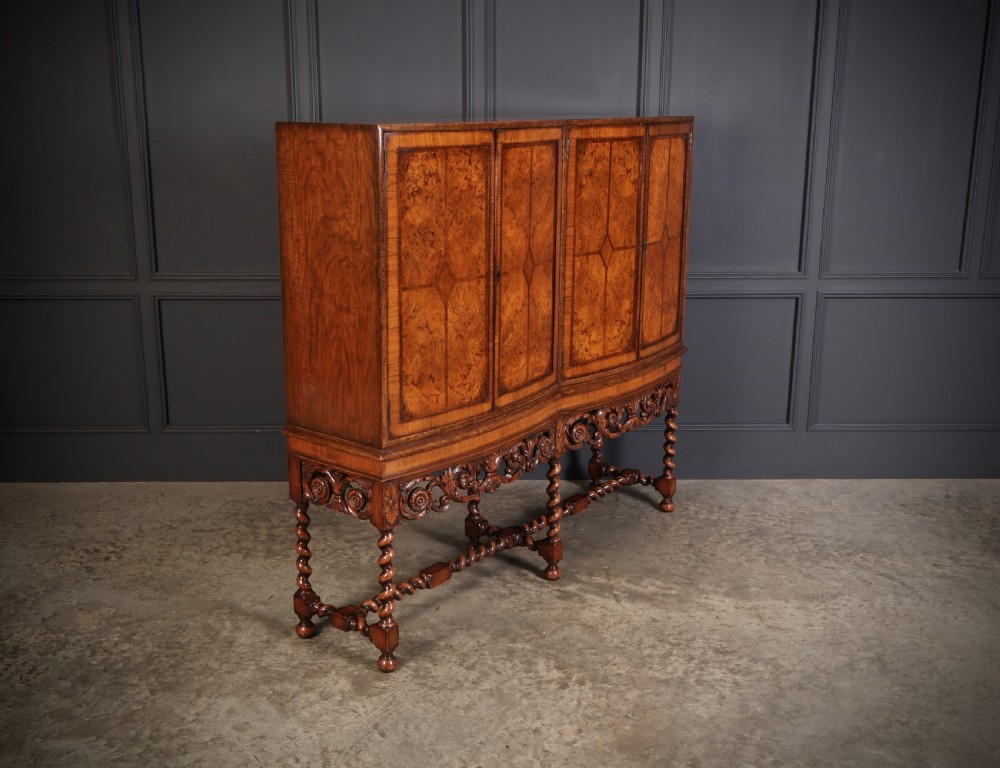 A double bow-front burr walnut cocktail cabinet featuring carved scrollwork on the lower apron, supported by six barley twist legs joined by stretchers. View III