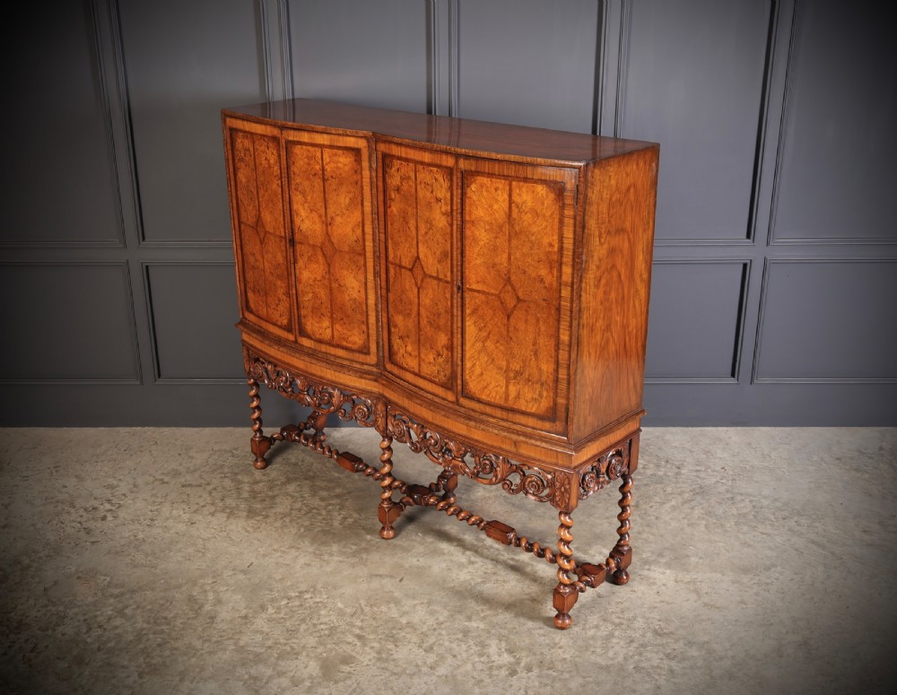 A double bow-front burr walnut cocktail cabinet featuring carved scrollwork on the lower apron, supported by six barley twist legs joined by stretchers. View IX