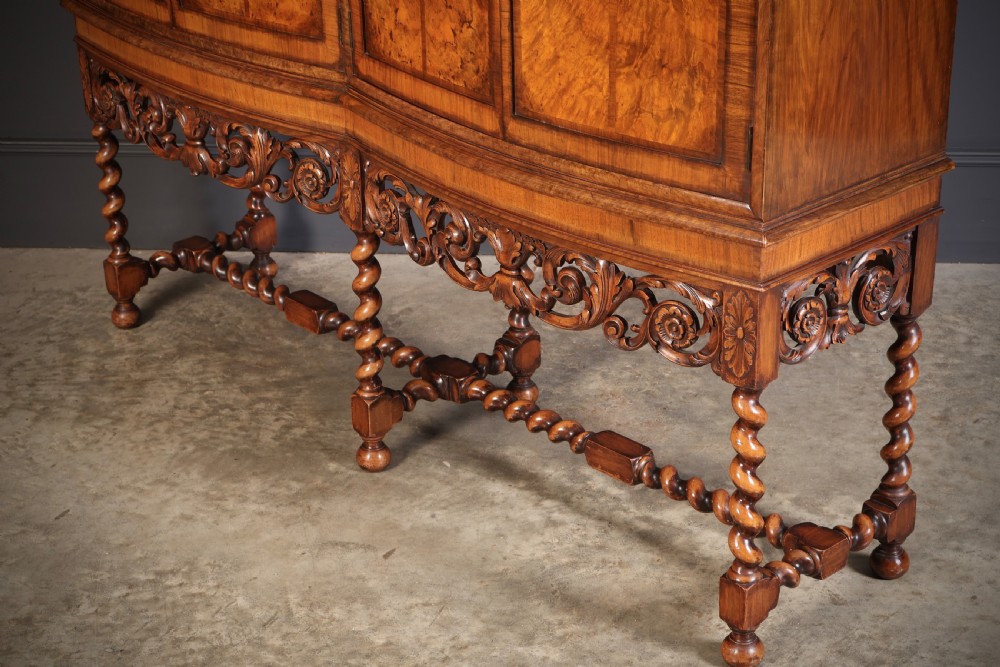 A double bow-front burr walnut cocktail cabinet featuring carved scrollwork on the lower apron, supported by six barley twist legs joined by stretchers. View X