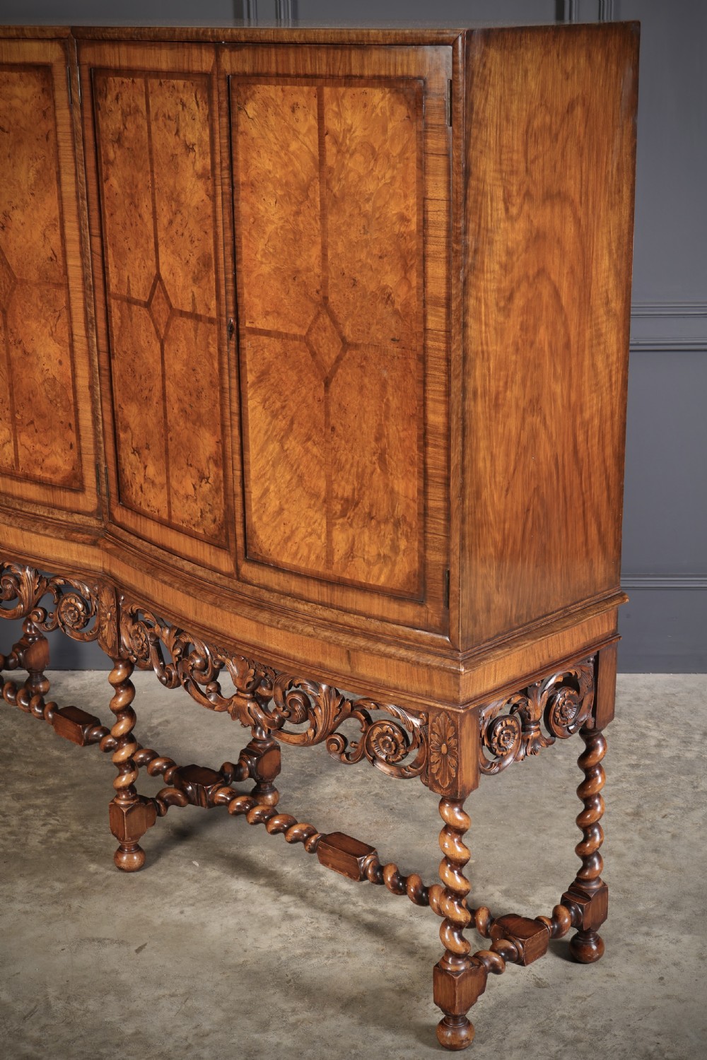 A double bow-front burr walnut cocktail cabinet featuring carved scrollwork on the lower apron, supported by six barley twist legs joined by stretchers. View XI