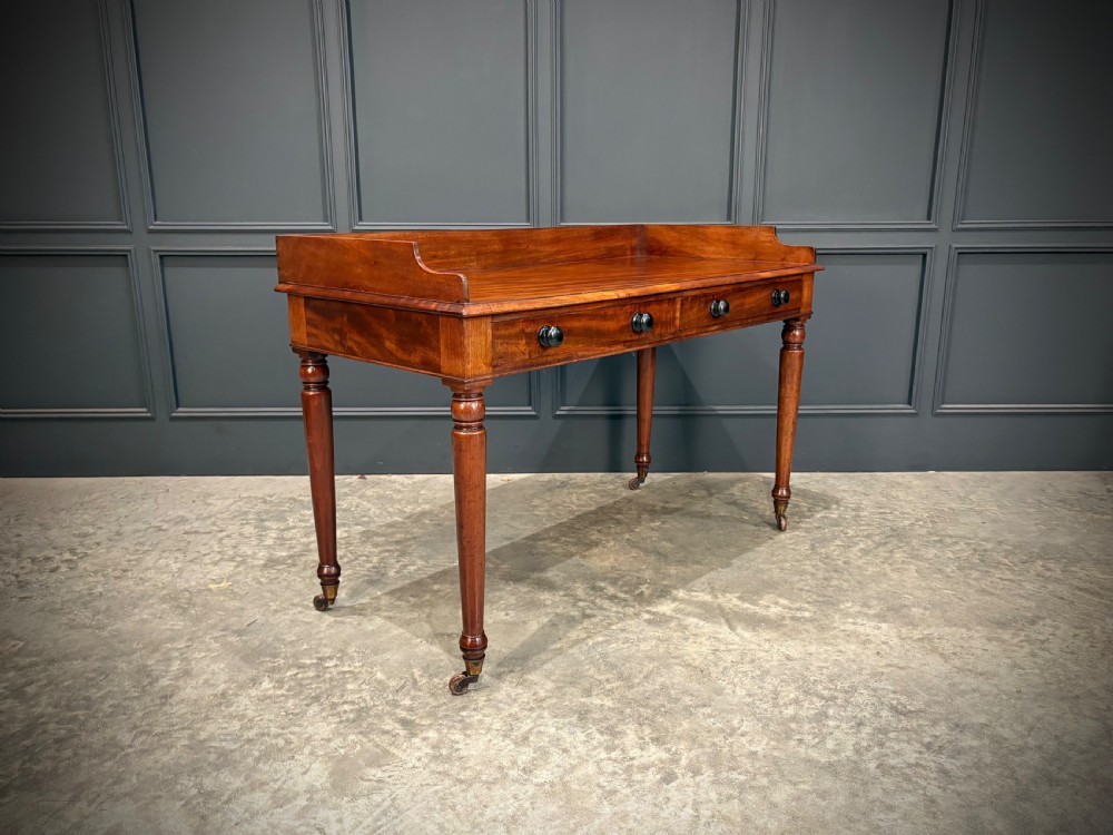 A William IV mahogany side table featuring a raised gallery back, two drawers with dark turned knobs, turned legs, and brass castors. View II