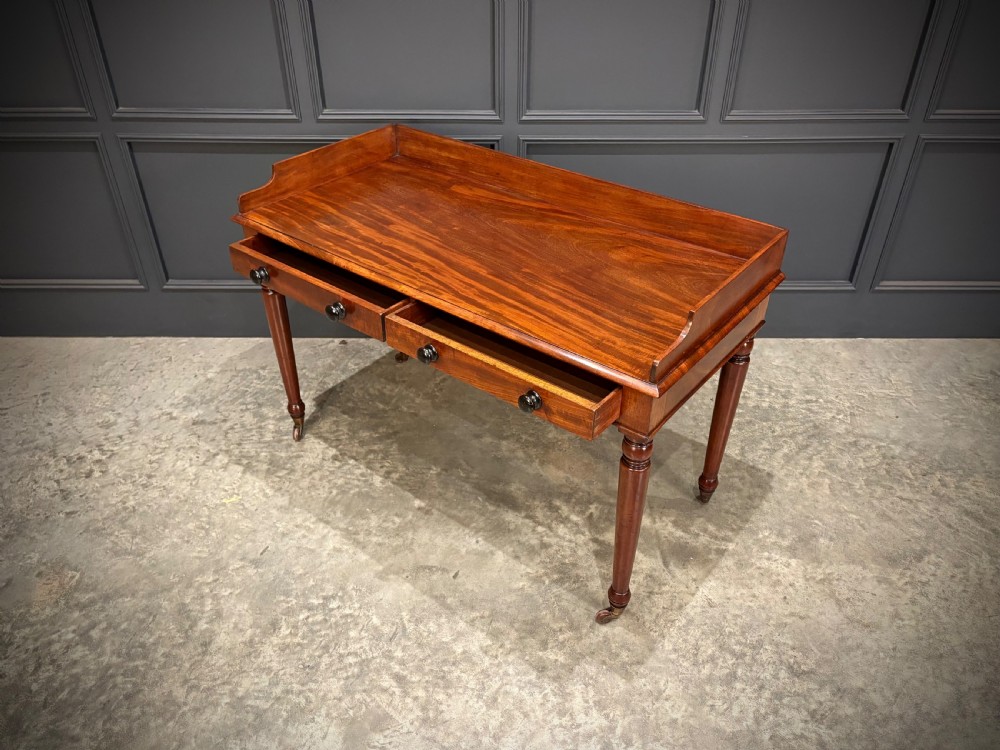 A William IV mahogany side table featuring a raised gallery back, two drawers with dark turned knobs, turned legs, and brass castors. View VIII
