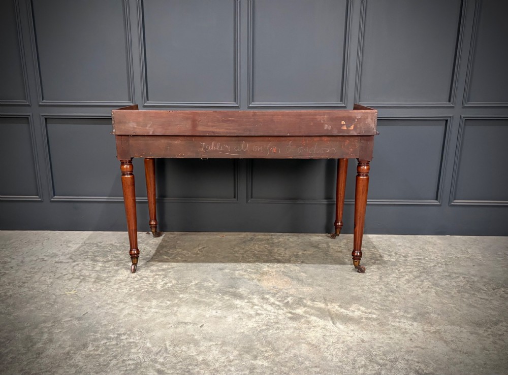 A William IV mahogany side table featuring a raised gallery back, two drawers with dark turned knobs, turned legs, and brass castors. View XI