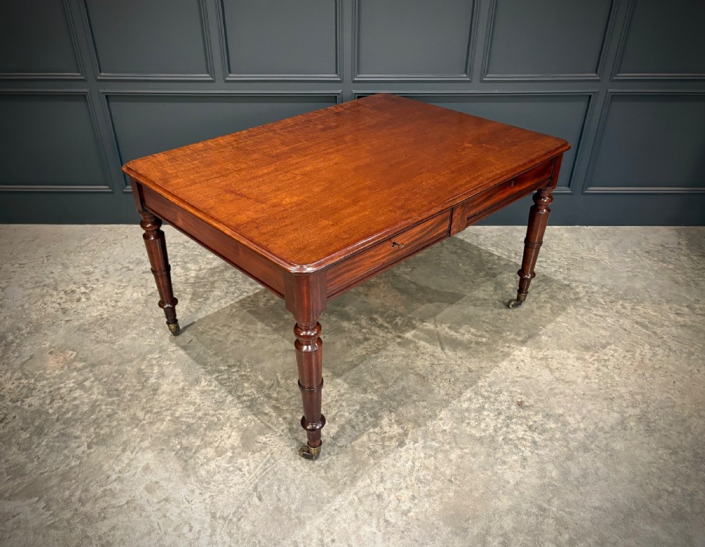 A rectangular Cuban mahogany library writing table featuring a polished wood top, frieze drawers with small keyholes, and turned legs with brass castors.